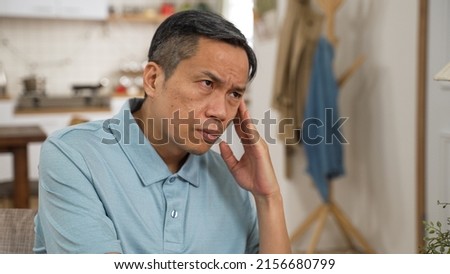 worried Japanese mature man having headache while considering hard decision alone at home. he stares into distance and shakes head feeling stressed out Royalty-Free Stock Photo #2156680799