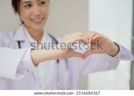 Beautiful young Doctor wearing coat and stethoscope smiling doing heart symbol shape with hands. Happy Surgeon Doctor Woman showing heart shape with hands.