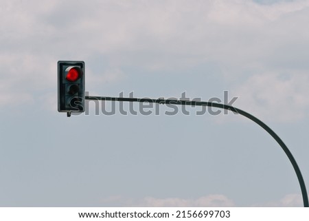 A low angle shot of Traffic lights with red light hanging on a black pole against the blue cloudy sky
