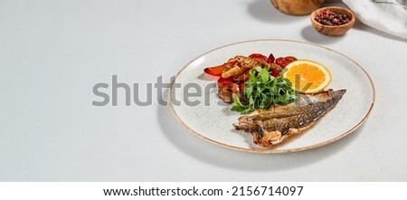 Fish dish - roasted dorado fillet with vegetables. Grilled fish fillet and roasted paprika, tomatoes and onion. Roast dorado fillet with garnish, greens and lemon on ceramic plate Royalty-Free Stock Photo #2156714097