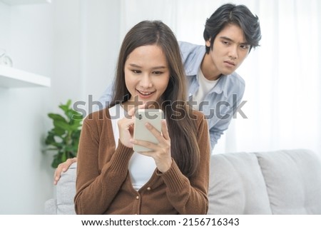 Infidelity, suspicion asian young couple love, wife using mobile phone, husband watching spying his girlfriend while woman chat a message, man sneaky distrust and jealousy, relationship problem. Royalty-Free Stock Photo #2156716343