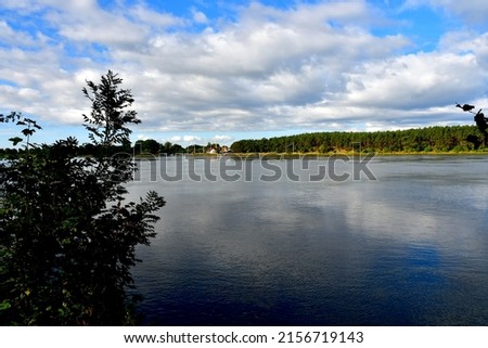 A view of a vast yet shallow lake covered from both sides with reeds, forests, moors, and other flora seen on a sunny yet cloudy summer day on a Polish countryside during a hike