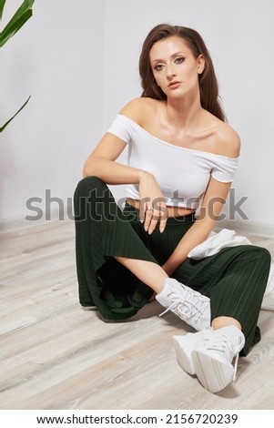 girl in a white T-shirt and green pants sitting on the floor