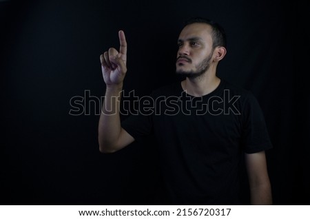 Latino caucasian man pointing to copy space on black background.