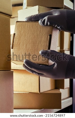 A worker man hands hold cardboard boxes on the shelves of a fully stocked warehouse. Warehouse overflowing with boxes of goods and postal parcels