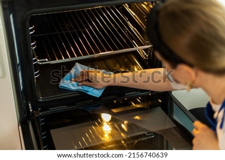 Cleaning lady in gloves washing oven in stylish kitchen. Close-up Royalty-Free Stock Photo #2156740639