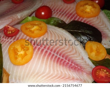 the process of cooking tilapia fish fillet with tomatoes, olives and lettuce leaves. High quality photo