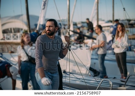 Preparation for the regatta at the yachting school at the marina with sailing yachts. Students and coaches prepare moored sports yachts for sailing on a sunny summer day. Royalty-Free Stock Photo #2156758907