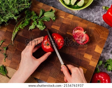 Cutting fresh tomato on wooden cutting board with Japanese knife. Making vegetable salad.