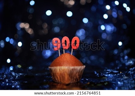 Tasty homemade vanilla anniversary cupcake with number 900 nine hundred on aluminium foil and blurred bright background in minimalistic style. Digital gift card birthday concept. High quality image
