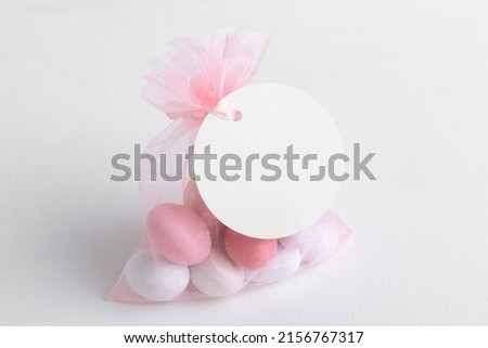 Round white tag mockup with gift with pink chocolate confetti in a bag with pink ribbon. Wedding favor tag for souvenir o gift for gues, sign for message greeting, close up, element for design