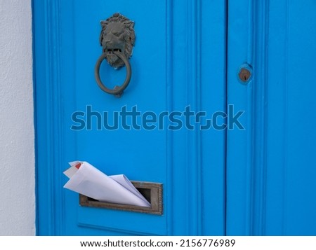 Blue vintage door with a knocker in the shape of a lion, mailbox slot in the door with advertising newspapers.