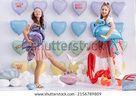 a cute little girls with balloons in the form of a heart in hands on many colorful heart balloons and big cake background. smiles,funny Valentine s Day birthday party
