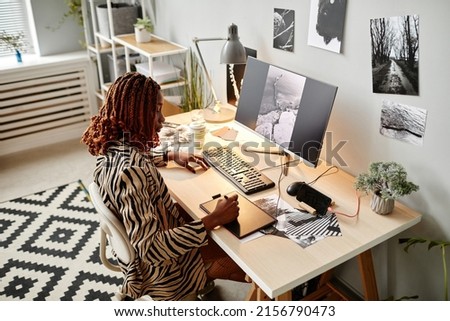 High angle portrait of black female creator editing photographs at home office workplace with graphic prints, copy space
