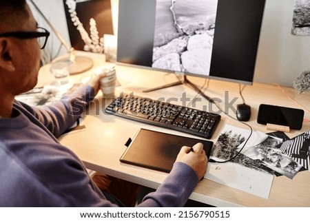 High angle portrait of male creator editing photographs at home office workplace and using pen tablet, copy space
