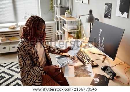 Side view portrait of black female creator holding photographs while choosing one for publishing, copy space