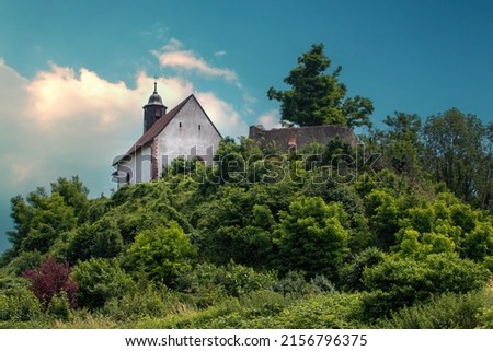 A scenic view of a church in a rural area surrounded by lush nature in cloudy sky background