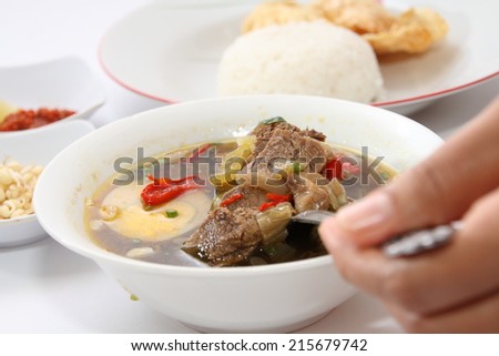 Rawon or Indonesian beef black soup, served with white rice, chili sauce and emping chips