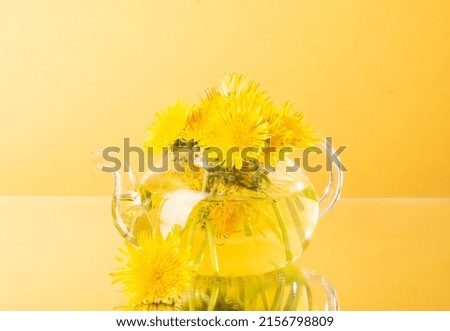 Dandelion flower tea in a glass teapot on a yellow background