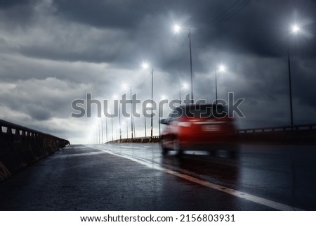 Blurry of car driving fast on bridge during hard rain with storm clouds as background,selective focus on ground and long shutter speed exposure.Concept of rainy season,transportation and travel.