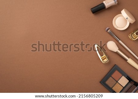 Makeup concept. Top view photo of eyeshadow palette gold barrettes nail polish and makeup brushes on isolated brown background with copyspace