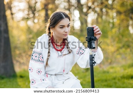 Ukrainian young blogger girl in national costume shooting some video on phone, while traveling in forest