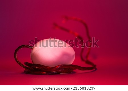 White egg with copper wire coming out on red illuminated background, concept of experiment hatching from an egg, abstract concept