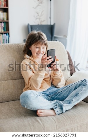Girl schoolgirl plays mobile phone sitting on the couch. Young blogger. social media