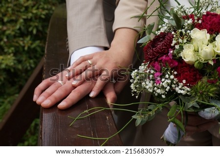Closeup of a married couple at the wedding with rings and flower bouquet. Bride and groom with beige brown colored clothes