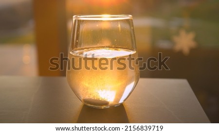 CLOSE UP: Effervescent tablet dissolving in sunlit glass of water. Sparkling beverage for regaining health backlit with beautiful golden light. Seasonal home treatment for immunity boost and health.