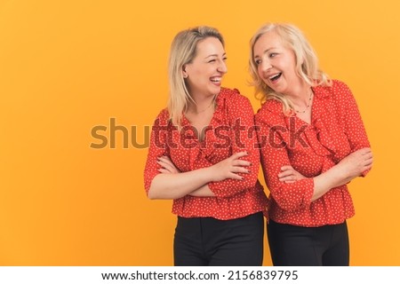 mom and her beautiful blonde daughter rejoicing and smiling while posing in the studio, copyspace isolated orange background. High quality photo