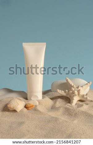 Sunscreen in white plastic tube. Photo shoot in the studio with blue background, sand, shells and white stones. Sunscreen with UVA and UVB protection. Summer atmosphere.