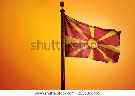 The national flag of North Macedonia on a flagpole isolated on an orange background