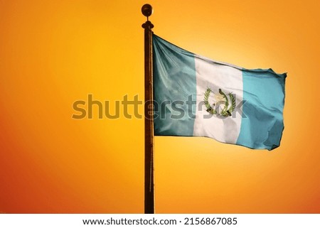 The national flag of Guatemala on a flagpole isolated on an orange background