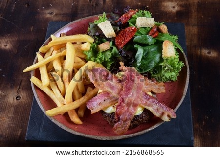lettuce salad of palm hearts tomato herbs vegetables and sauce, hamburger bacon and french fries healthy food