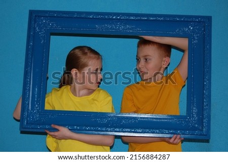 a boy and a girl with red hair in yellow T-shirts look at each other and hold a blue frame on a blue background in their hands