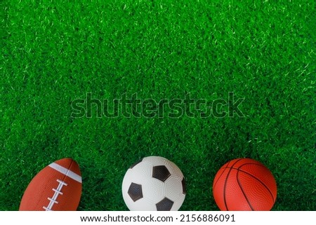 Top view of soccer, basketball and football balls on green grass background.