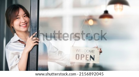 Smiley asian female barista holding open board sign standing at her shop.