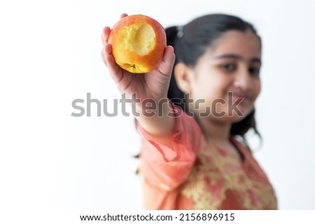 Portrait of cute Pakistani little girl showing a bitten apple against white background, selective focus