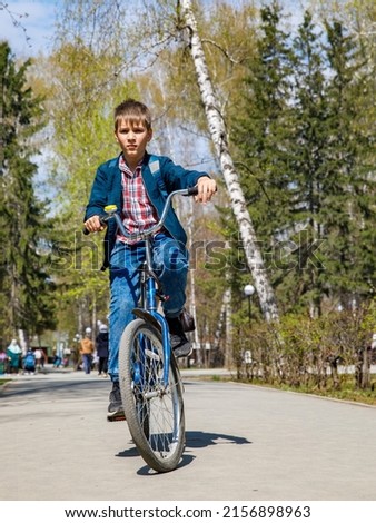 Healthy lifestyle - teen school boy with backpack riding bicycle in city park in spring sunny day. Going to school or having leisure in summer park. Vertical