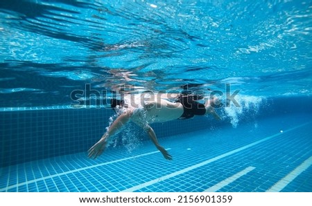 underwater photo of A man who swims and dives in the pool, does activities, exercises and takes care of her health. with fun swimming