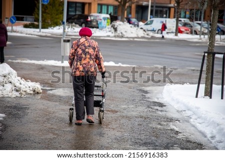 An elderly woman walking with the help of a walker in a snowy winter Royalty-Free Stock Photo #2156916383