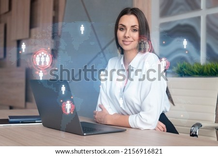 Attractive businesswoman in white shirt at workplace working with laptop to hire new employees for international business consulting. HR, social media hologram icons over office background