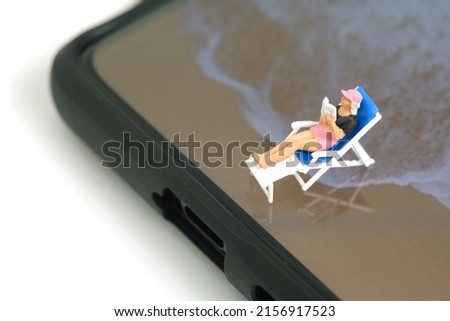 Miniature people toy figure photography. Virtual travel concept, a girl relaxing at beach seat while reading a book above smartphone, isolated on white background. Image photo