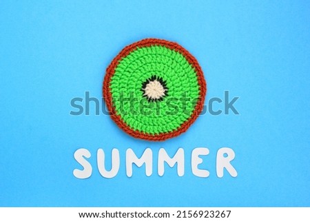 Colourful crochet slice of kiwi and lettering Summer on blue background. Hello Summer vacation creative tropical bright minimalistic fresh food concept. Flatlay, top view holiday composition