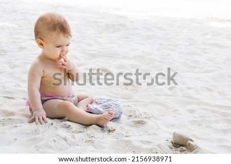 Cute little baby girl in pink swimming trunks playing sand at beach. Sensory development for kids outdoors. Royalty-Free Stock Photo #2156938971