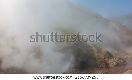 The hillside is shrouded in thick steam from an erupting geyser. Poor visibility due to haze. Kamchatka. Valley of Geysers Royalty-Free Stock Photo #2156939265