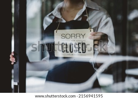 Asian young woman notice sign wood board label "SORRY WE ARE CLOSED PLEASE COME BACK AGAIN" hanging through glass door front shop, Business close during coronavirus pandemic disease concept