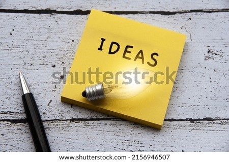 Ideas text with light bulb on notepad. Wooden desk and pen background