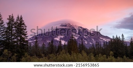 A white cloud sitting on top of a high mountain covered with snow